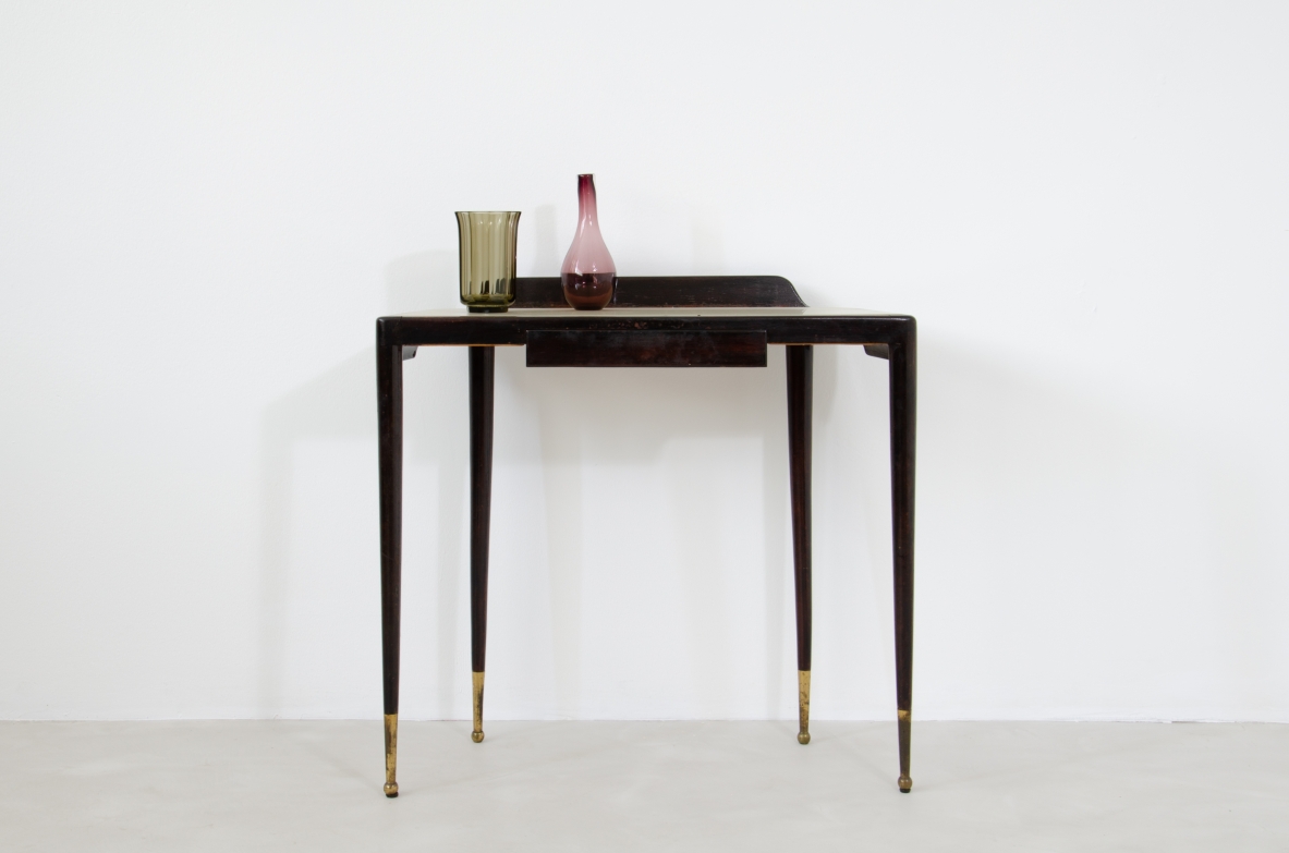 Elegante console con sottili gambe in legno tinto e lunghi puntali in ottone. Cassetto centrale e piano in vetro opaline color avorio.  Manifattura Italiana 1950ca.