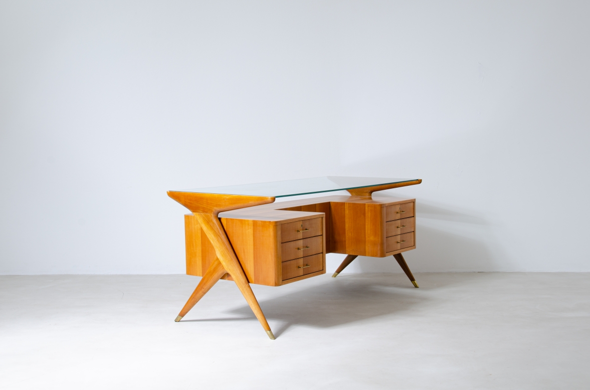 Scrivania in legno biondo con piano in vetro di grande spessore e montanti laterali sagomati con puntali in ottone,.  Manifattura italiana 1950ca.