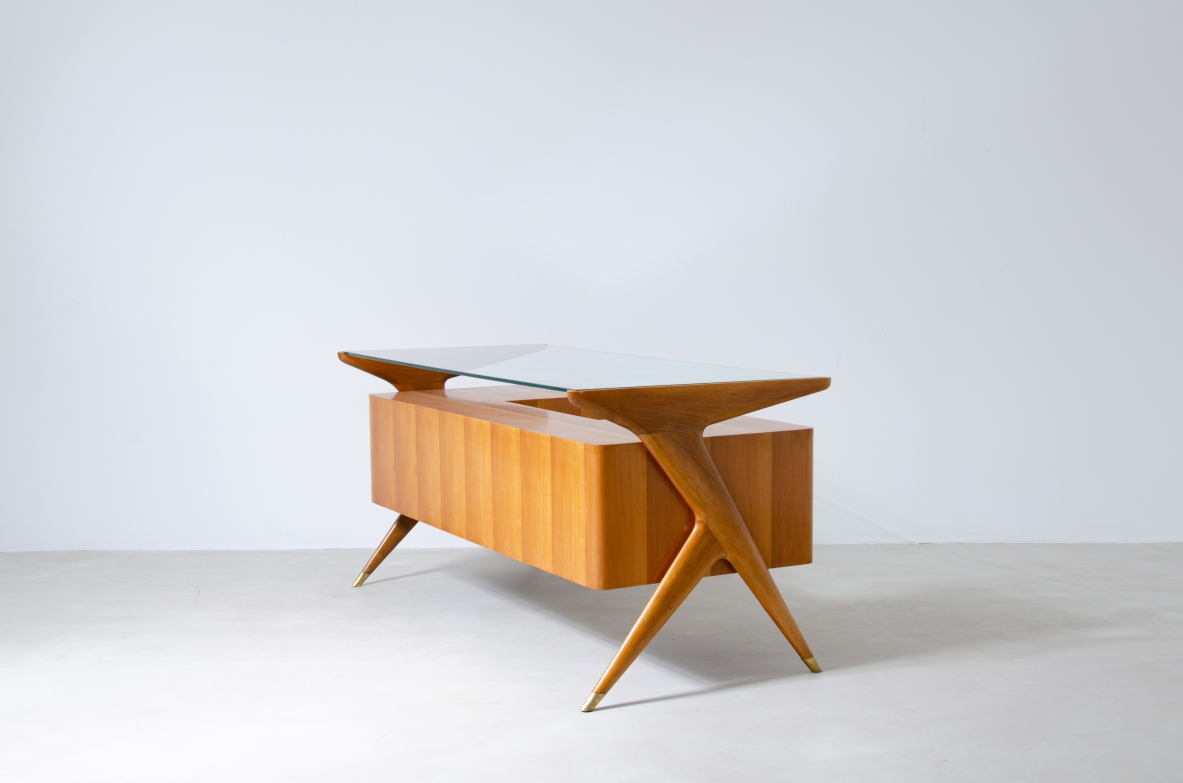 Scrivania in legno biondo con piano in vetro di grande spessore e montanti laterali sagomati con puntali in ottone,.  Manifattura italiana 1950ca.