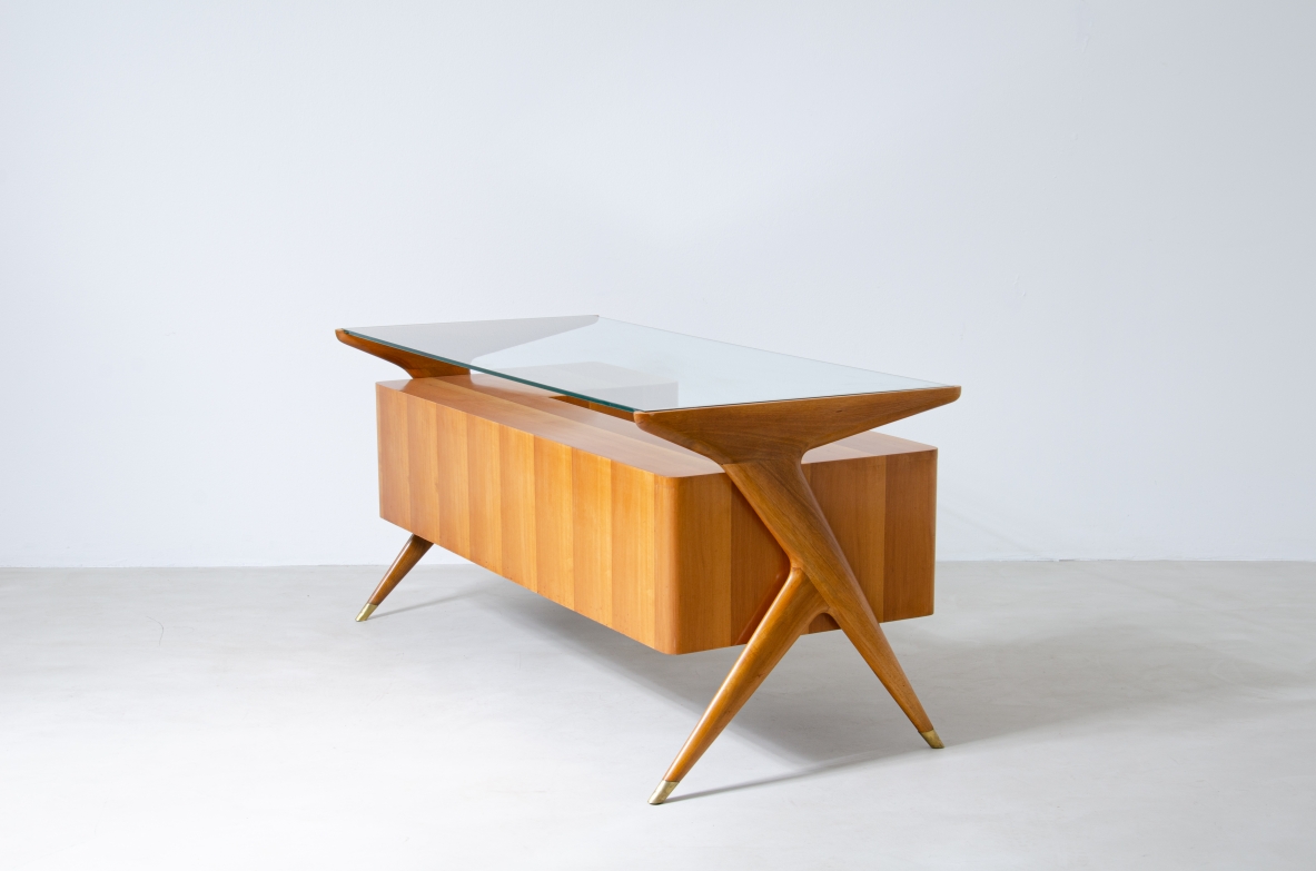 Scrivania in legno biondo con piano in vetro di grande spessore e montanti laterali sagomati con puntali in ottone,.  Manifattura italiana 1950ca.