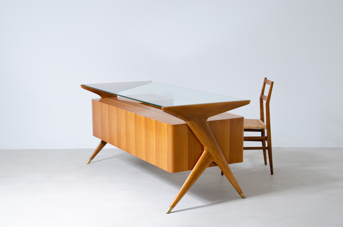 Scrivania in legno biondo con piano in vetro di grande spessore e montanti laterali sagomati con puntali in ottone,.  Manifattura italiana 1950ca.