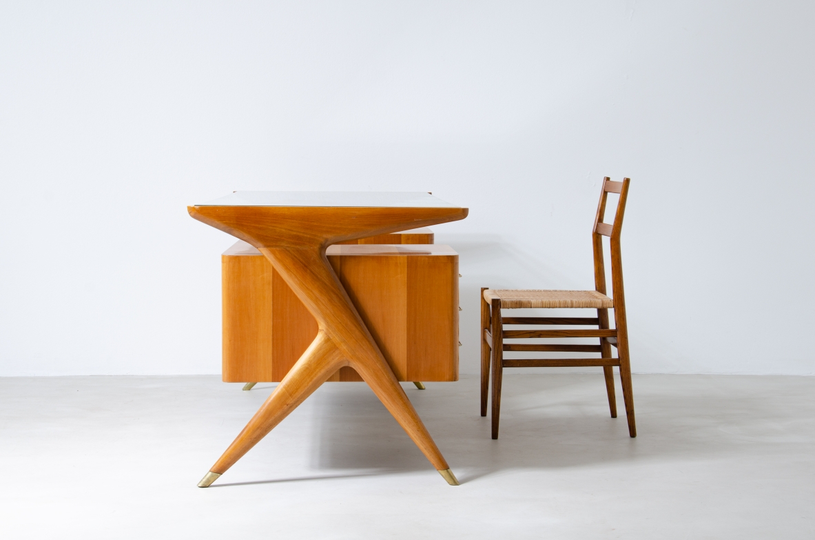 Scrivania in legno biondo con piano in vetro di grande spessore e montanti laterali sagomati con puntali in ottone,.  Manifattura italiana 1950ca.