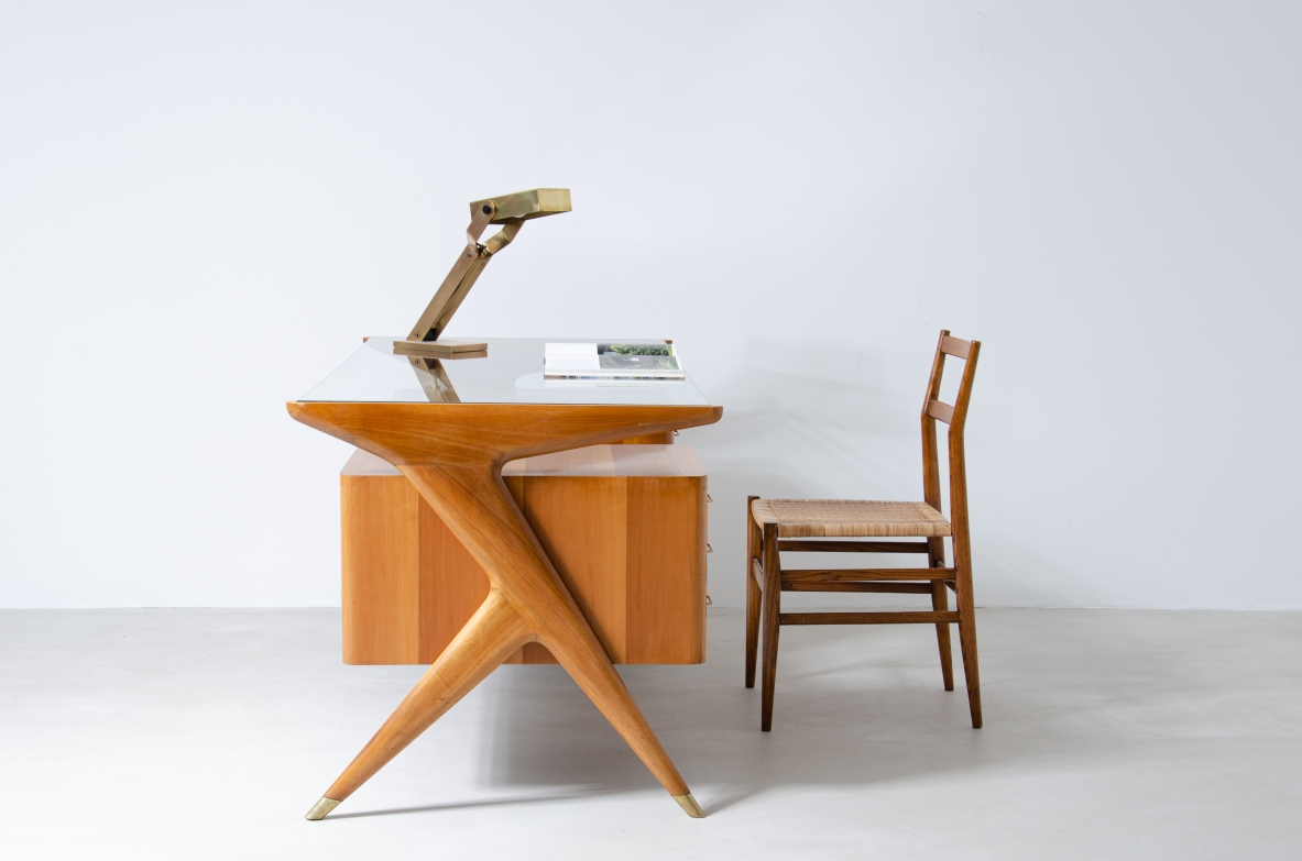 Scrivania in legno biondo con piano in vetro di grande spessore e montanti laterali sagomati con puntali in ottone,.  Manifattura italiana 1950ca.