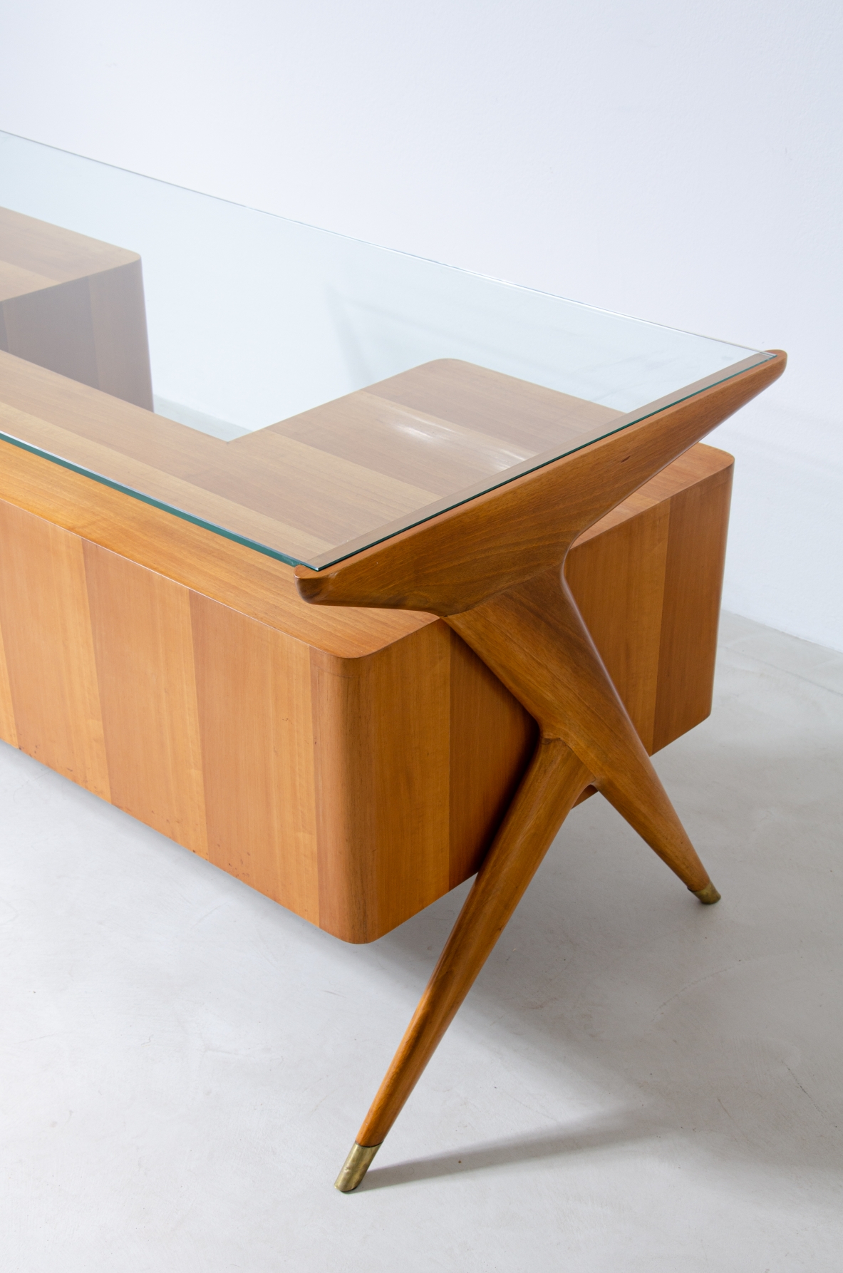 Scrivania in legno biondo con piano in vetro di grande spessore e montanti laterali sagomati con puntali in ottone,.  Manifattura italiana 1950ca.