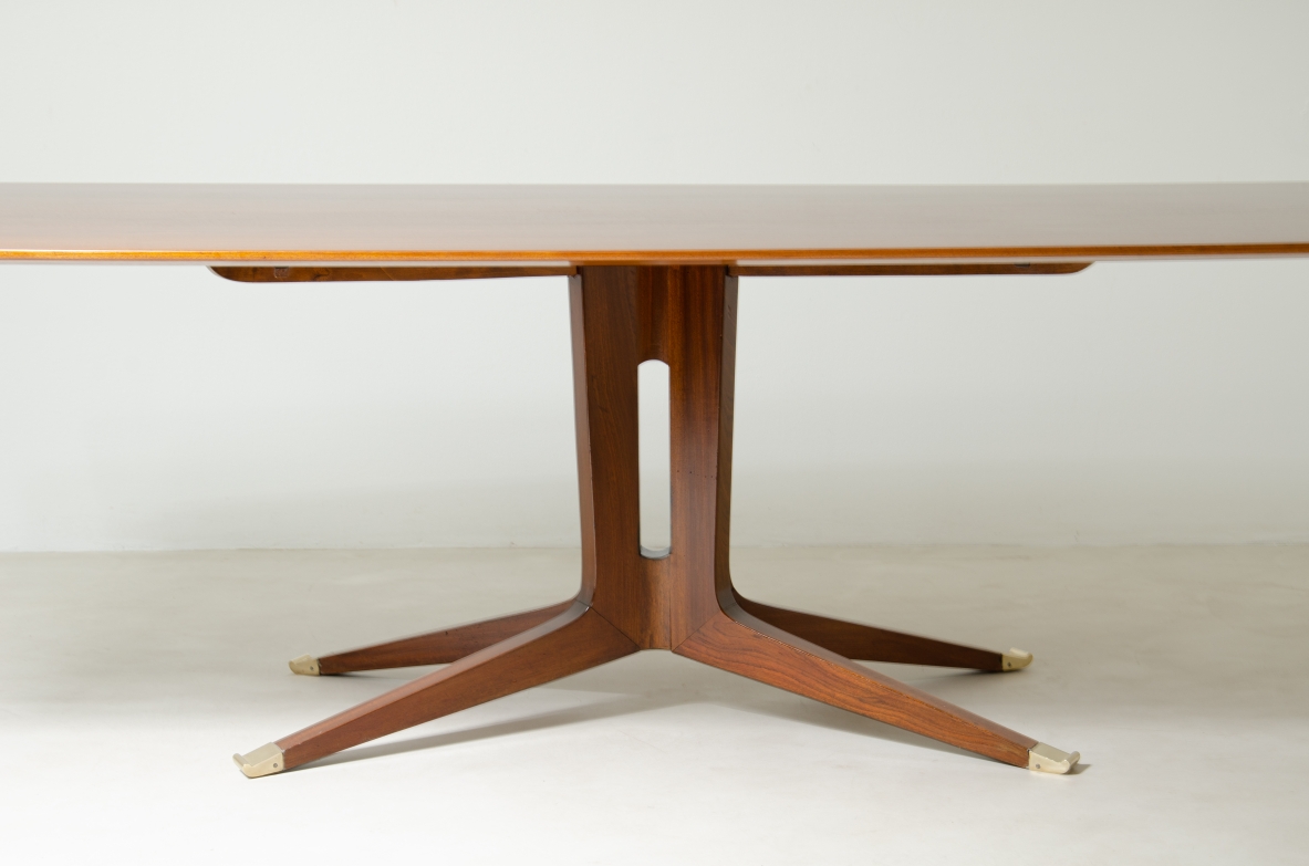 Grande tavolo in mogano con piano sagomato e gamba con fusto centrale e quattro razze con elegante puntale in ottone.  Manifattura italiana 1950ca.