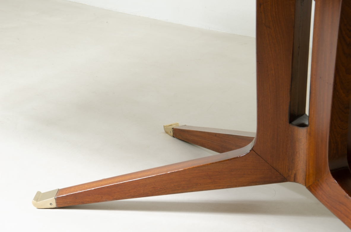 Grande tavolo in mogano con piano sagomato e gamba con fusto centrale e quattro razze con elegante puntale in ottone.  Manifattura italiana 1950ca.