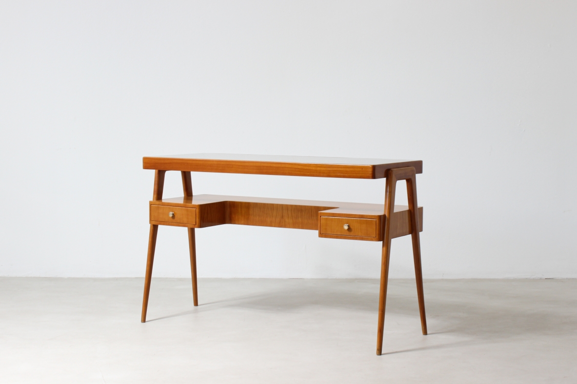 Piccolo scrittoio in legno biondo con piano in vetro e ripiano sagomato con due cassetti sul fronte.