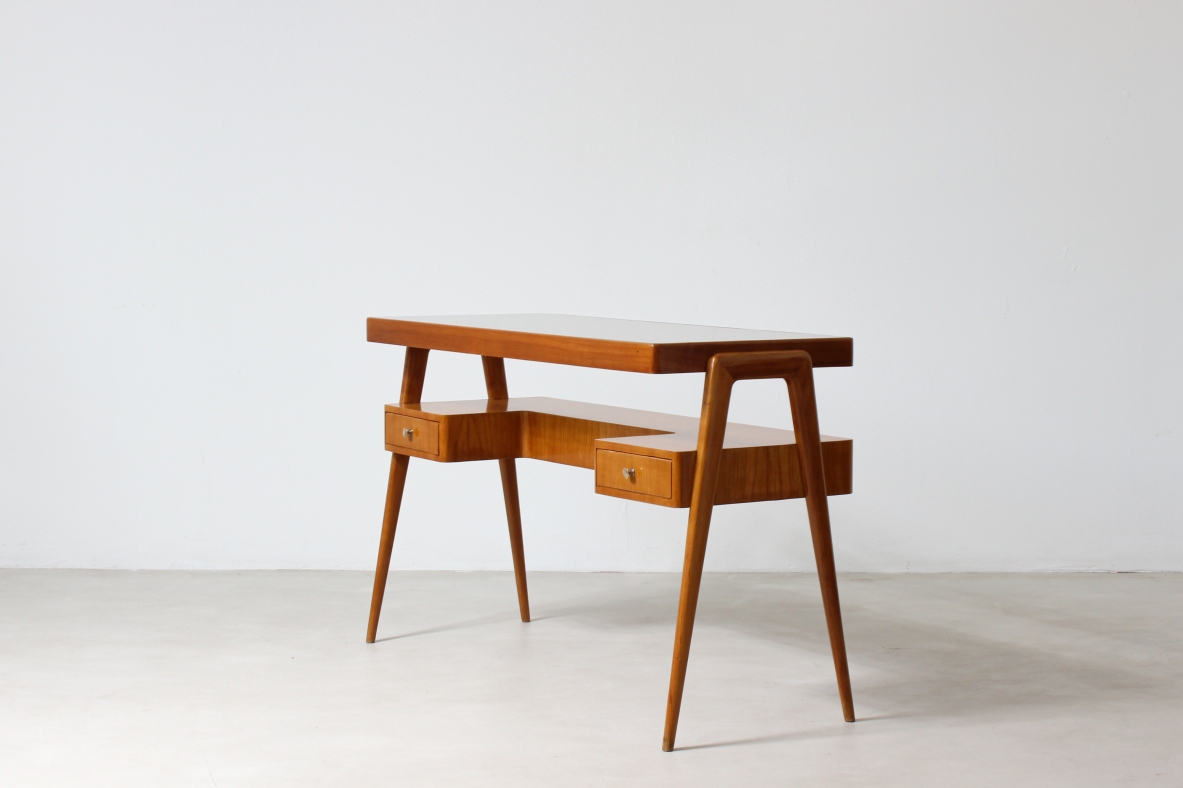 Piccolo scrittoio in legno biondo con piano in vetro e ripiano sagomato con due cassetti sul fronte.