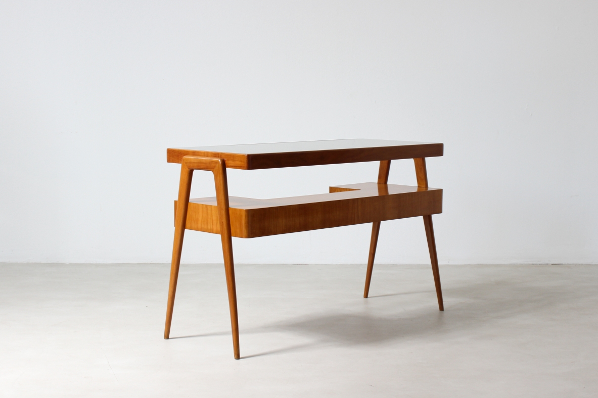 Piccolo scrittoio in legno biondo con piano in vetro e ripiano sagomato con due cassetti sul fronte.