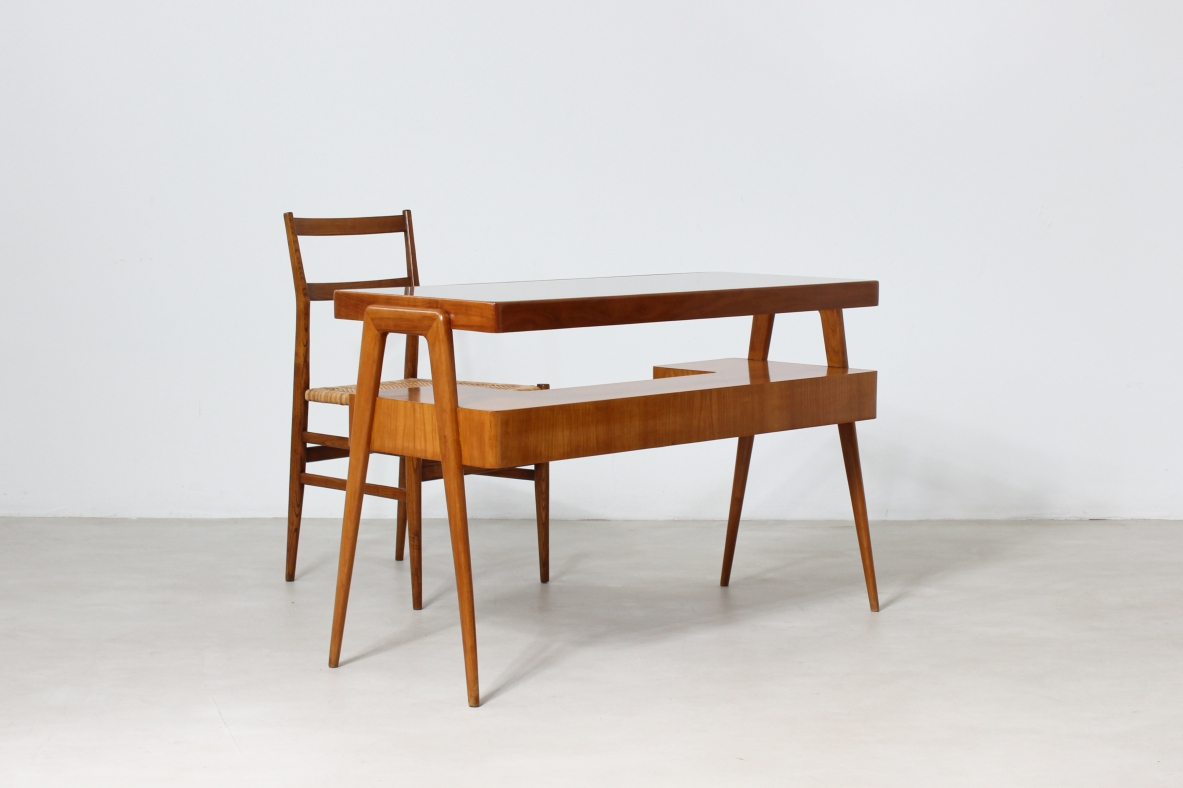 Piccolo scrittoio in legno biondo con piano in vetro e ripiano sagomato con due cassetti sul fronte.