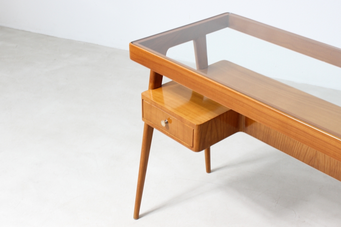 console in legno biondo con piano in vetro e ripiano sagomato con due cassetti sul fronte.