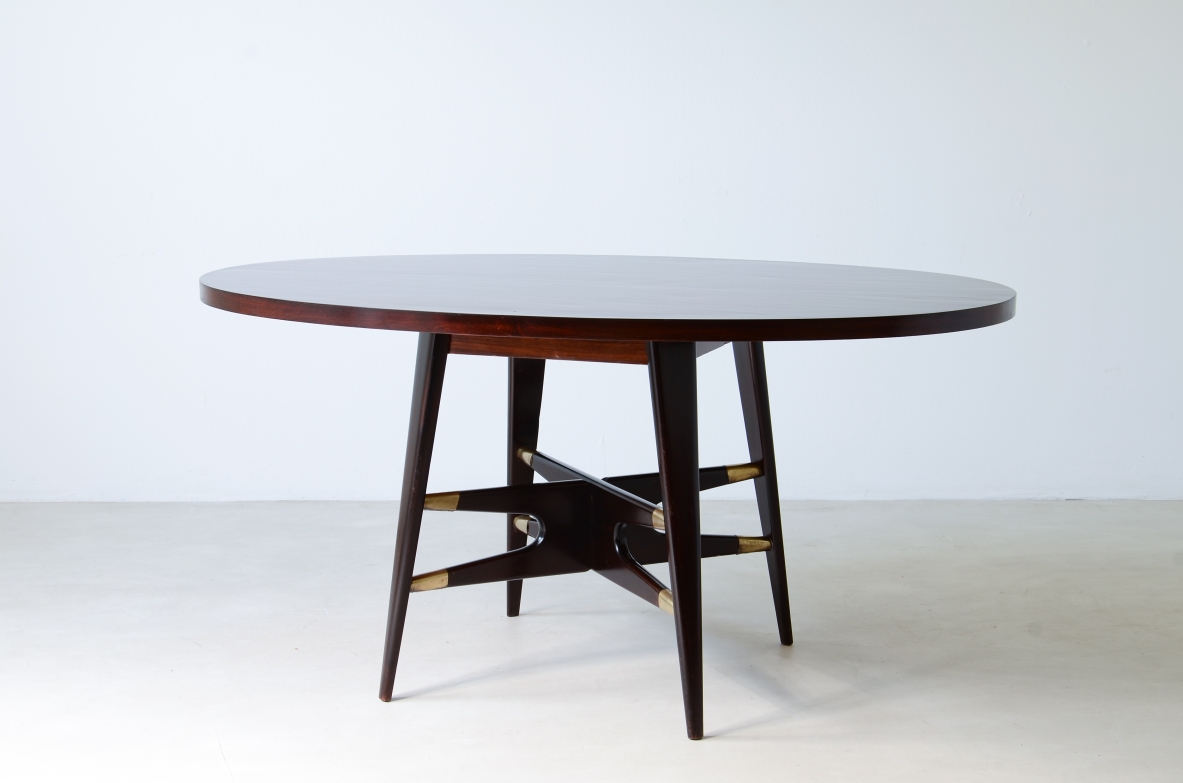 Gianni Vigorelli   Elegante tavolo ovale in legno tinto con montanti a quattro gambe e importante crociera con puntali in ottone.  Manifattura italiana, attr. Vigorelli. 1950ca.
