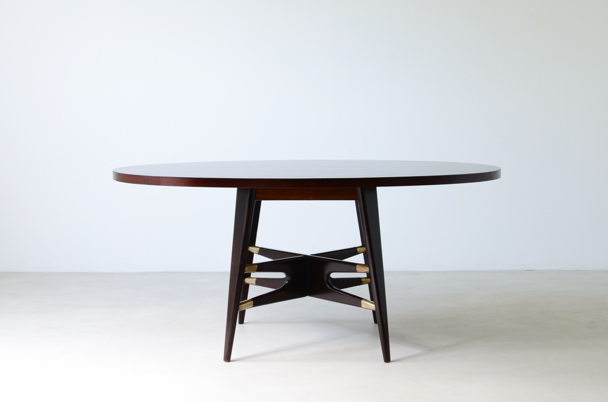 Gianni Vigorelli   Elegante tavolo ovale in legno tinto con montanti a quattro gambe e importante crociera con puntali in ottone.  Manifattura italiana, attr. Vigorelli. 1950ca.