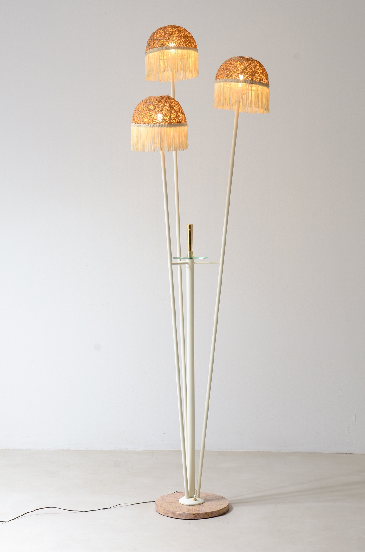 Lampada da terra a tre bracci in metallo laccato con cappelli in rattan e frange in tessuto.Manifattura italiana 1950ca.